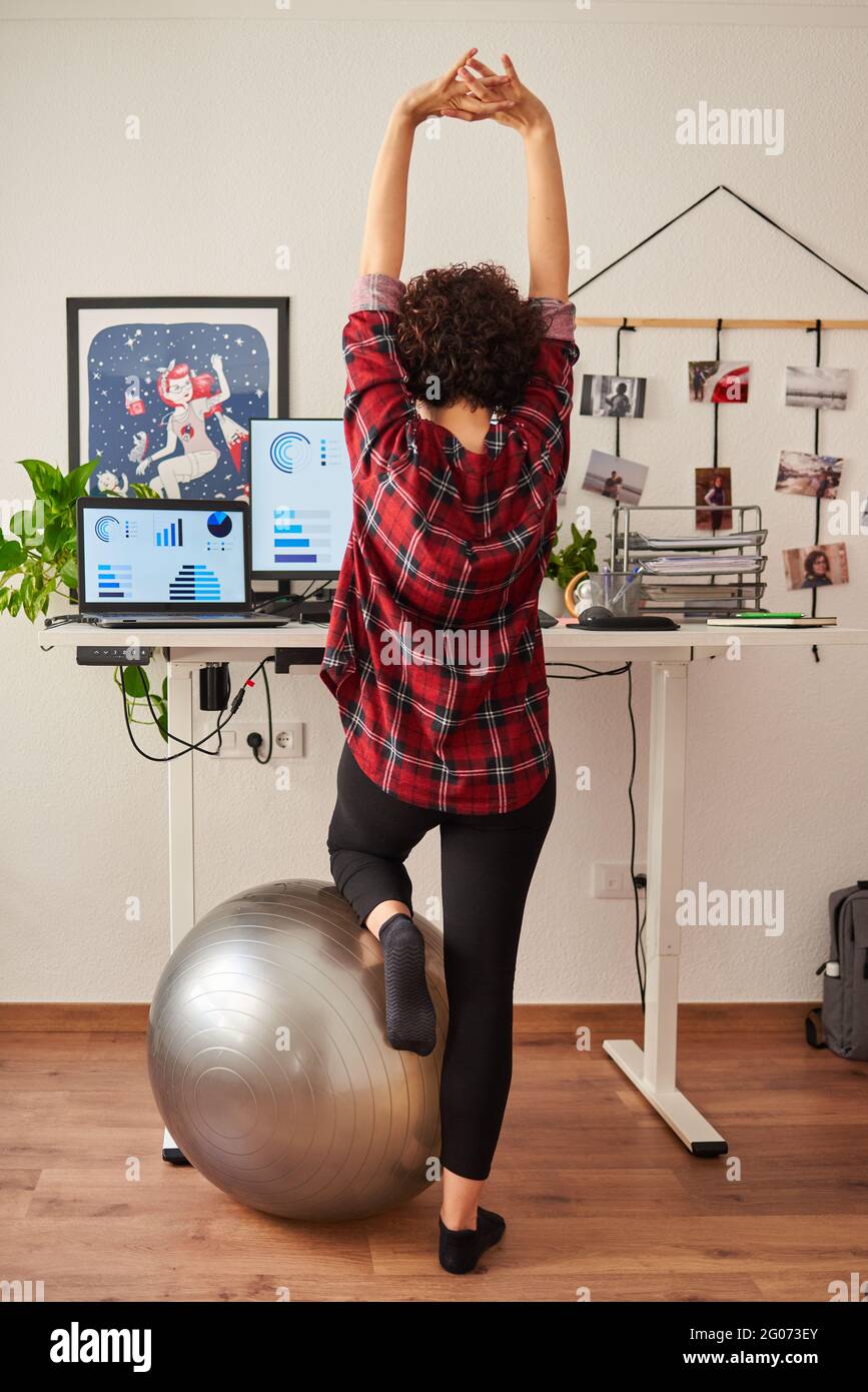 Donna che telelavoro su una scrivania regolabile in piedi accanto a a. montare la sfera Foto Stock