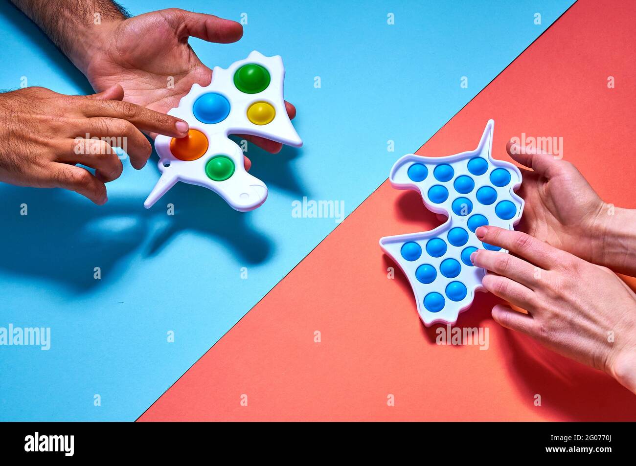 Le mani di uomo e donna si allungano verso i giocattoli colorati trendy e semplici, a concavità su sfondo blu. Foto Stock