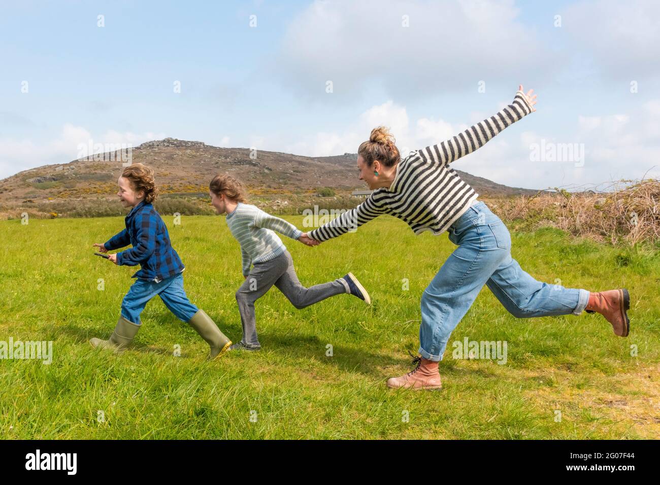 Una madre e i suoi figli si divertono a correre in un campo nella zona di West Penwith in Cornovaglia. Foto Stock