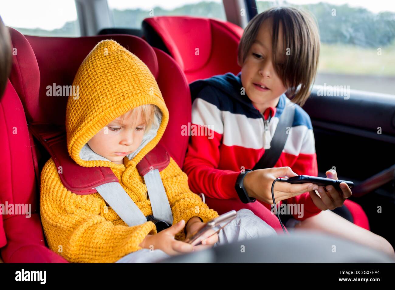 Tre bambini, ragazzi, che viaggiano in auto in carseat e giocano sui cellulari per abbreviare il tempo Foto Stock