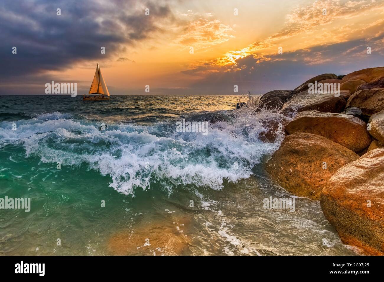 Una barca a vela sta navigando lungo l'Oceano Tramonto mentre UN'onda si tuffa sulla riva Foto Stock