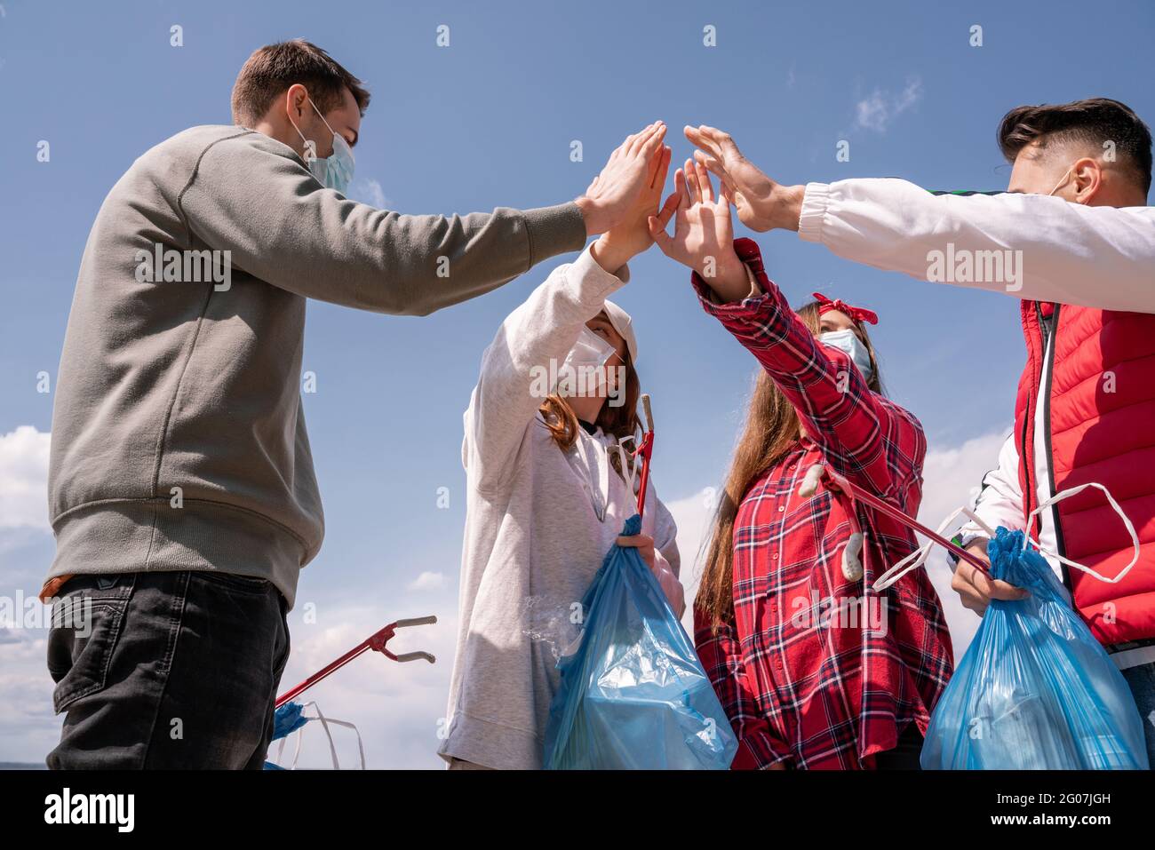 giovani donne e uomini in maschere mediche che tengono sacchetti di spazzatura e tenendo insieme le mani, pick up concetto di spazzatura Foto Stock