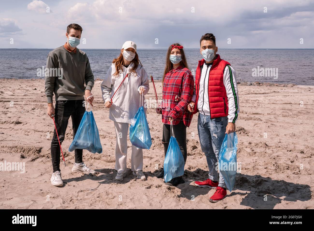 giovani donne e uomini in maschere mediche che tengono sacchi di spazzatura e grabbers all'esterno, pick up concetto di spazzatura Foto Stock