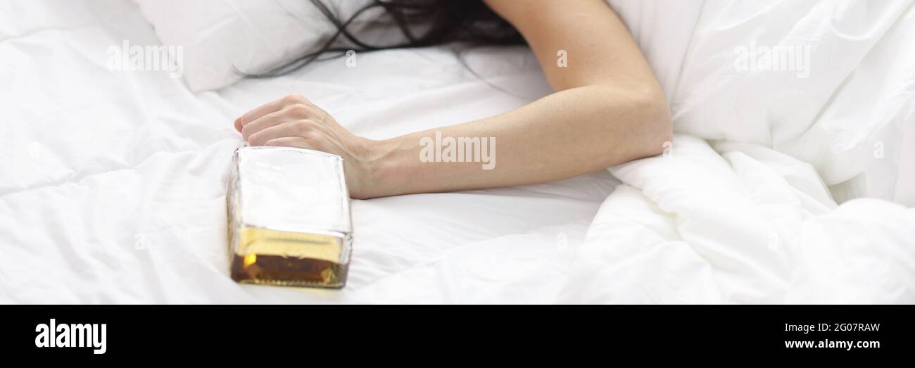 Donne sdraiate in letto bianco con una bottiglia di whisky mano Foto Stock
