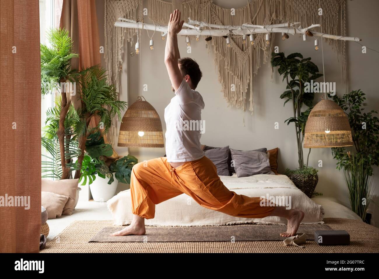 uomo che pratica yoga facendo la posa guerriero o virabhadrasana a casa Foto Stock