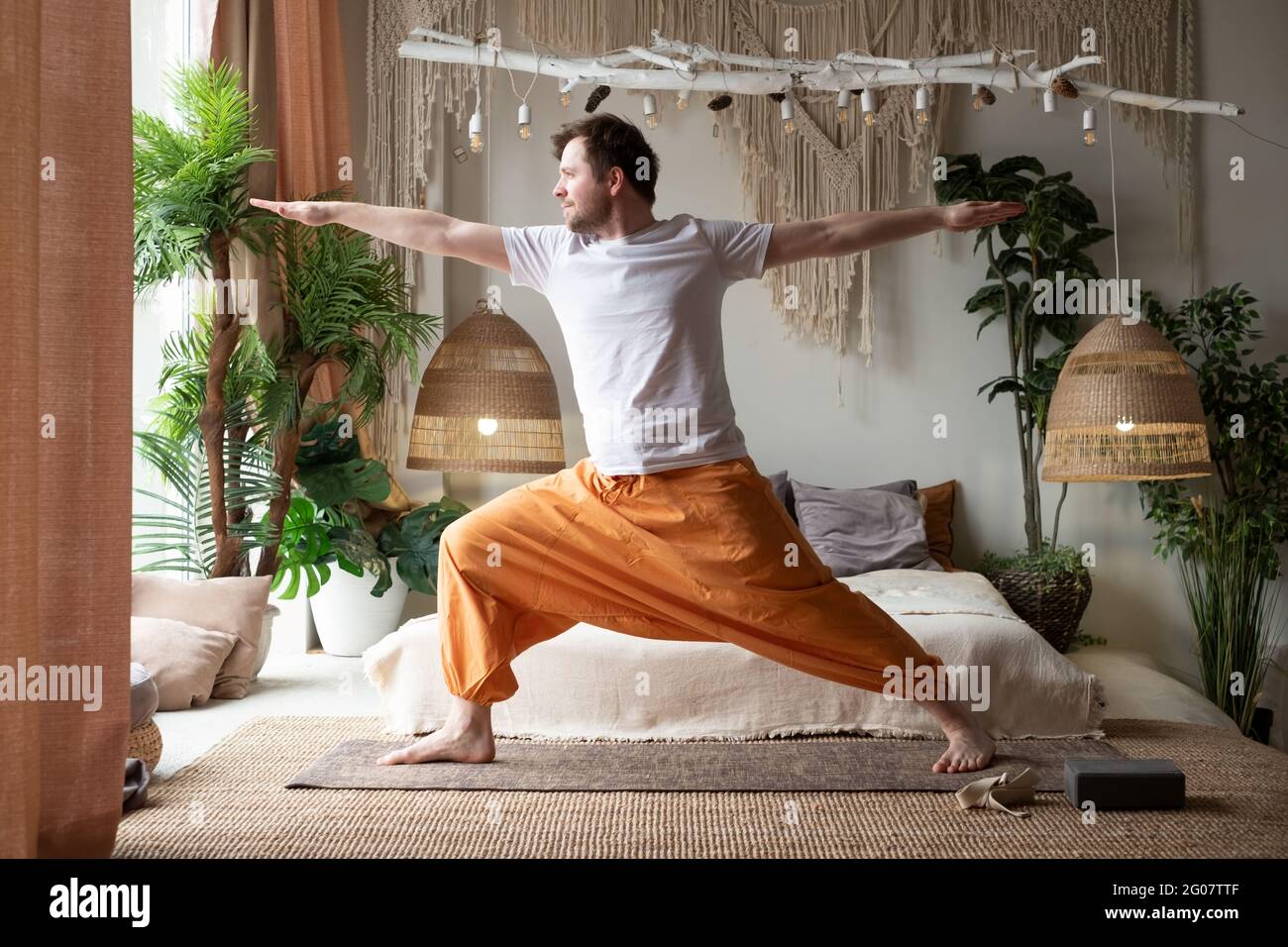 uomo che pratica yoga facendo la posa guerriero o virabhadrasana a casa Foto Stock