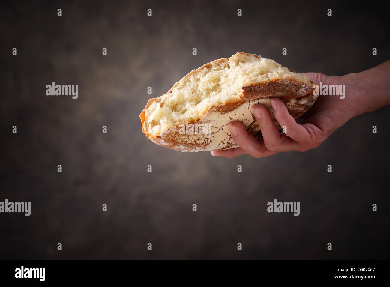 Mano che dà un pezzo di pane su sfondo grigio scuro marrone. Concetto di aiuto, gesto dell'umanità, primo piano, spazio per il testo. Foto Stock