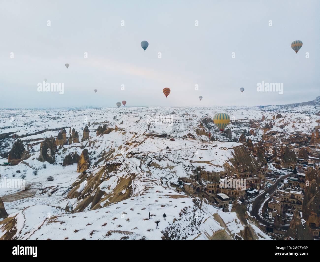 Incredibile vista sui droni dei colorati mongolfiere che volano sopra Antico insediamento di Uchisar e terreno roccioso innevato con spettatori Fredda giornata invernale a Cappa Foto Stock