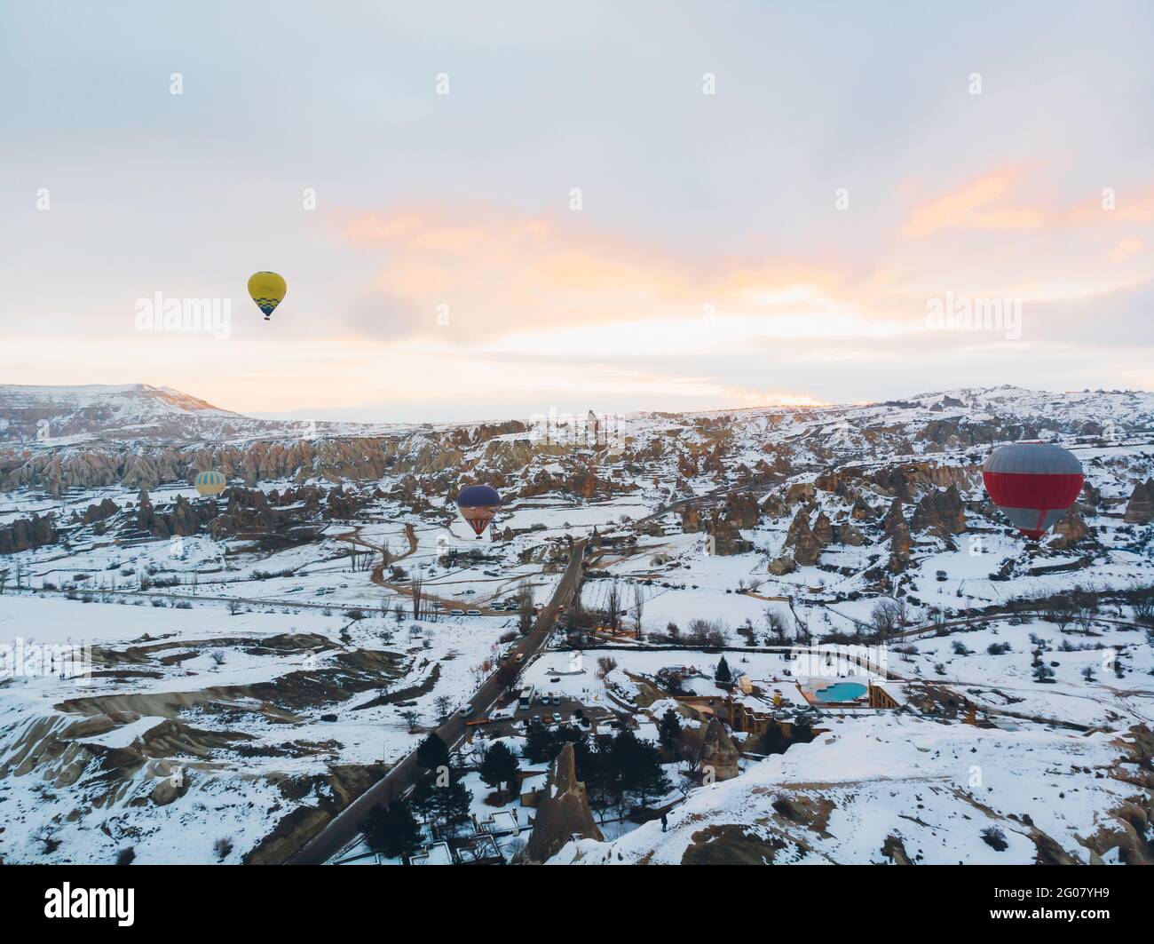 Incredibile vista sui droni dei colorati mongolfiere che volano sopra Antico insediamento di Uchisar e terreno roccioso innevato con spettatori Fredda giornata invernale a Cappa Foto Stock