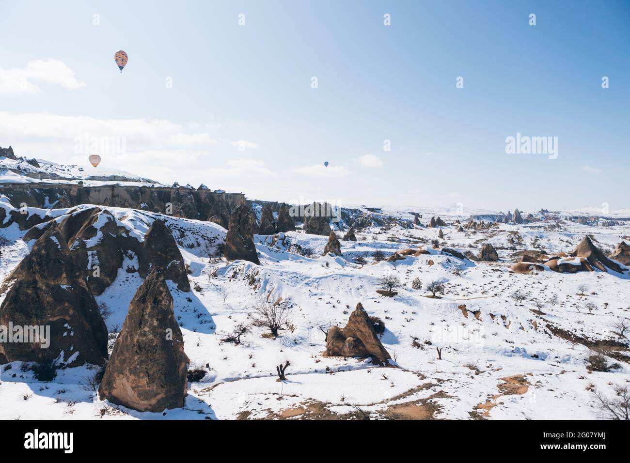 Incredibile vista sui droni dei colorati mongolfiere che volano sopra Antico insediamento di Uchisar e terreno roccioso innevato con spettatori Fredda giornata invernale a Cappa Foto Stock