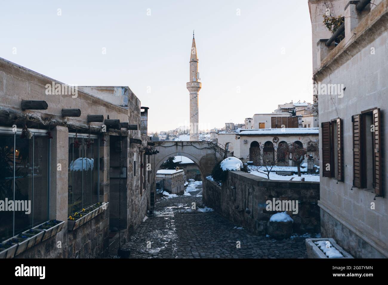 Strada vuota con pietre di pavimentazione che conduce tra gli edifici antichi a. Alta torre minareto contro il cielo blu chiaro in Turchia in periodo invernale Foto Stock