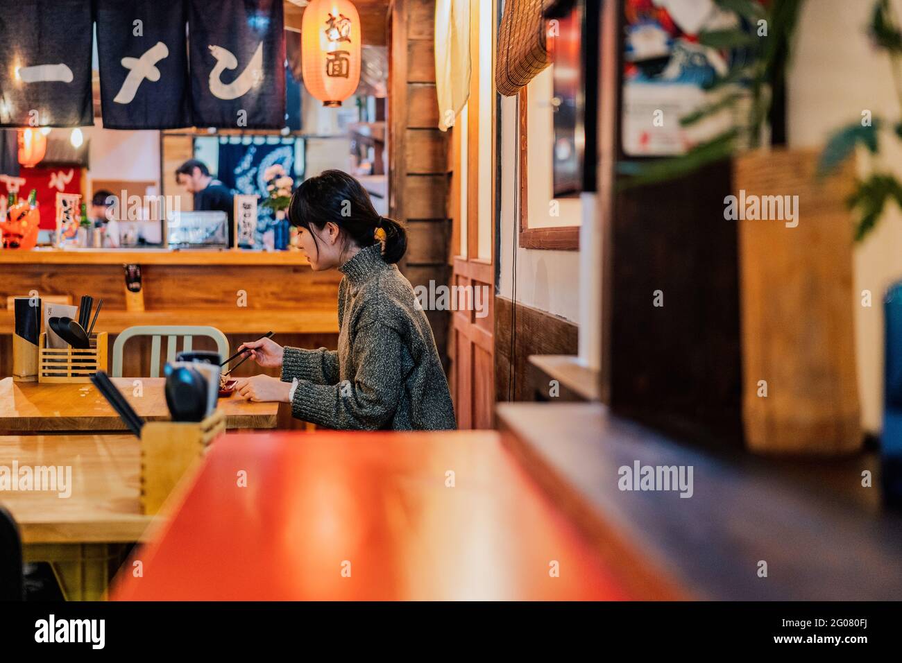Giovane donna asiatica in maglione mangiare al bancone in legno nel caffè Foto Stock