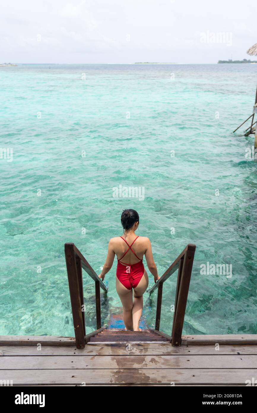 Vista posteriore della donna anonima in costume da bagno che scende scale  in acqua rilassante alle Maldive Foto stock - Alamy