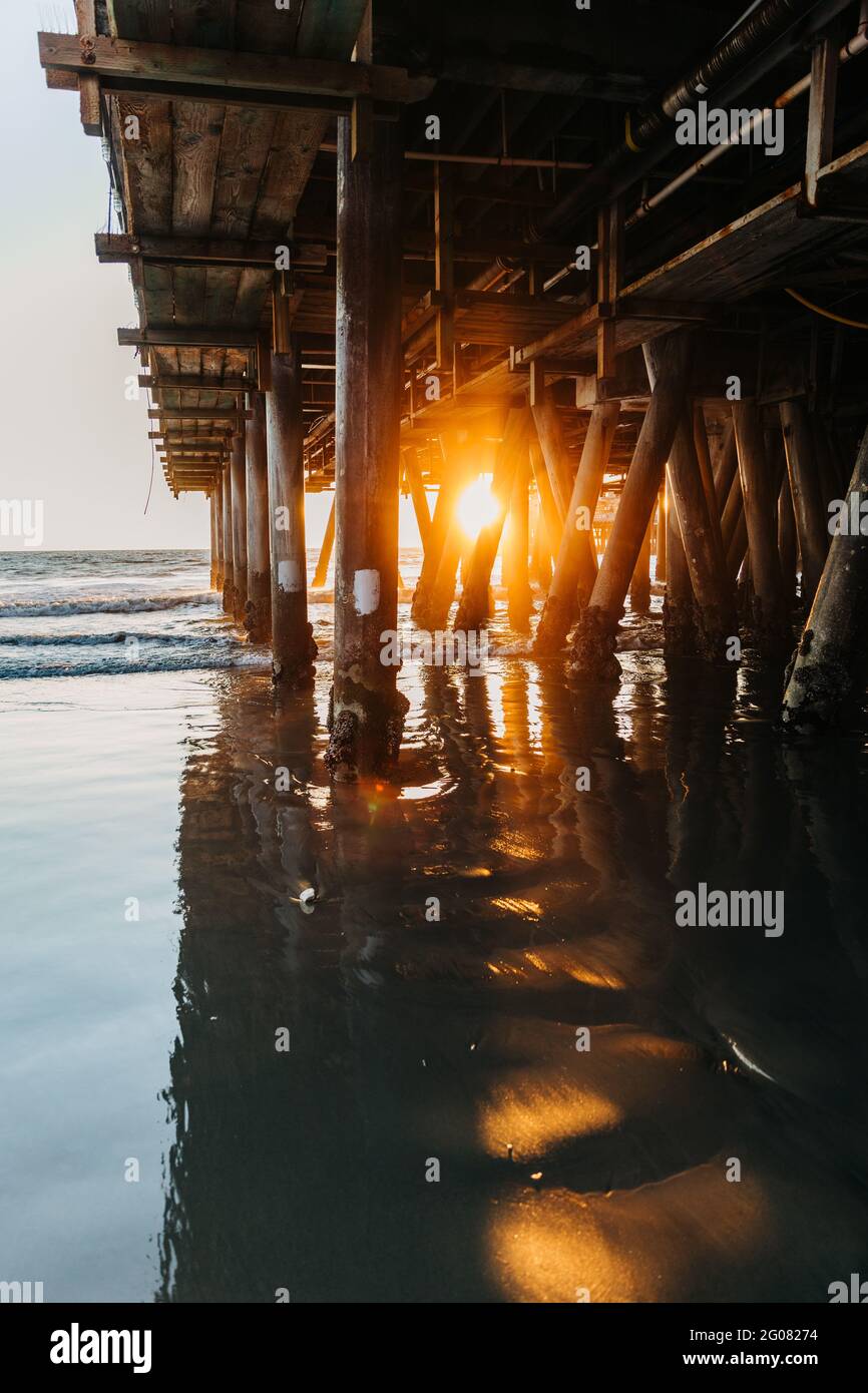 Luce solare incandescente alla sera penetrando mucchi di Santa Monica molo con tranquille onde oceaniche che corrono sulla spiaggia in California Foto Stock