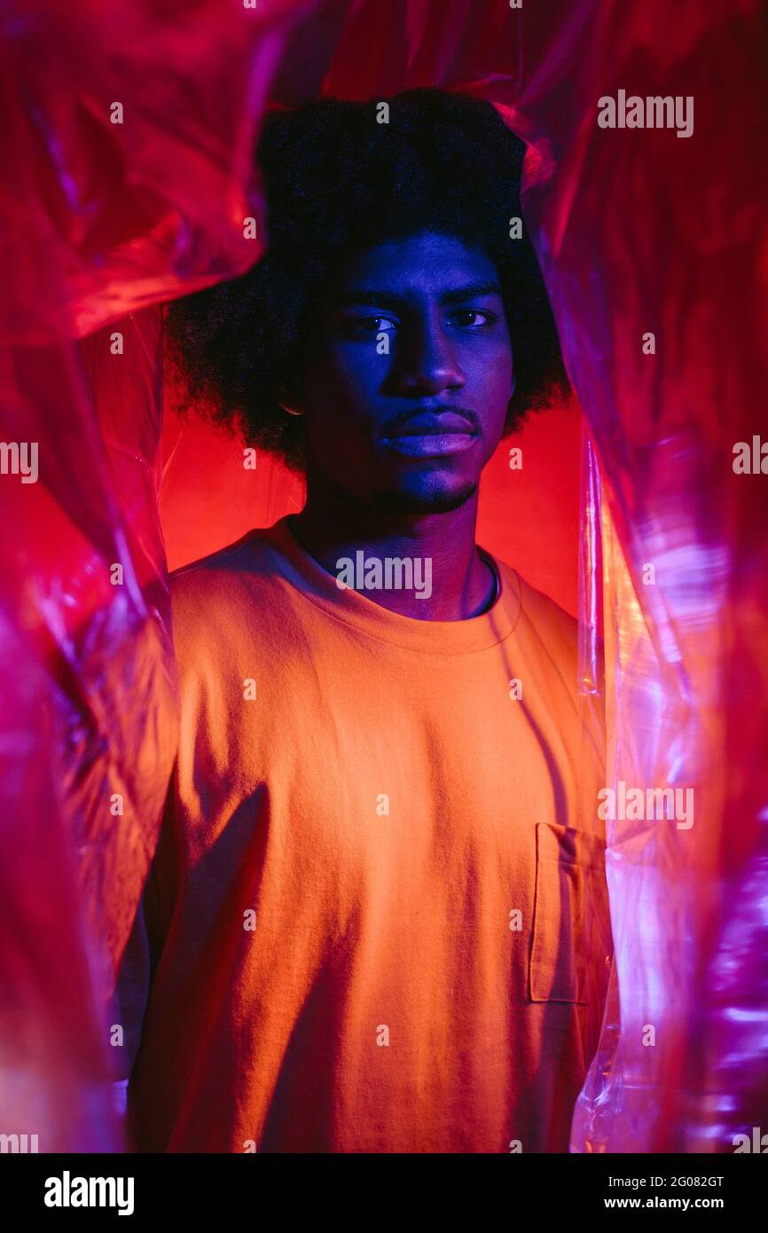 Giovane uomo afroamericano calmo con capelli afro casual vestiti sotto il  cellophane trasparente di plastica guardando la macchina fotografica contro  sfondo rosso Foto stock - Alamy