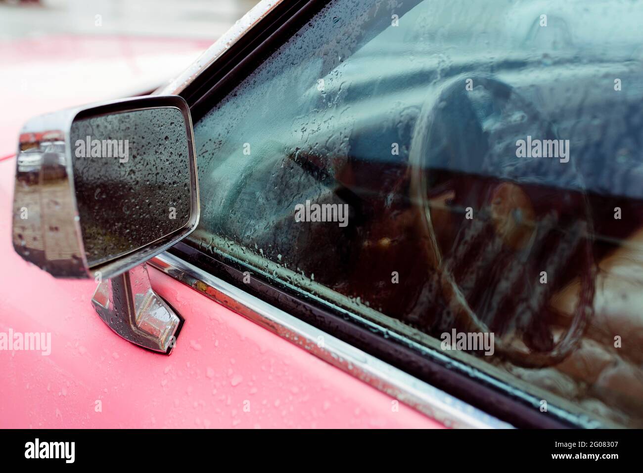 Dettaglio di uno specchio retrovisore di un classico rosa auto in una giornata piovosa Foto Stock