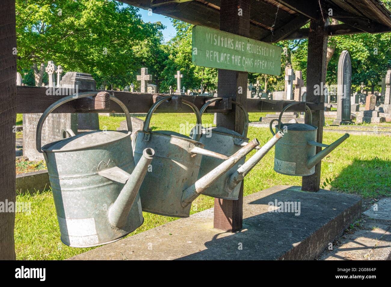 Le lattine per innaffiatura in metallo pendono su una rastrelliera nel cimitero di Hanwell per i visitatori di utilizzare il fiore d'acqua. Foto Stock