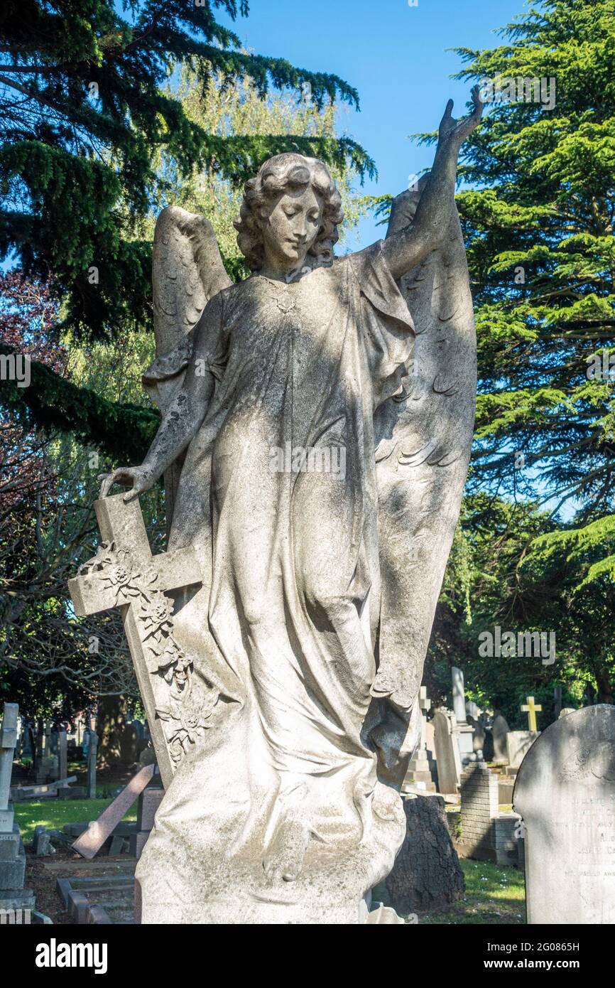 Una scultura di una figura angelica, una signora che tiene una croce fa parte di una lapide nel cimitero di Hanwell a Londra, Regno Unito. Foto Stock