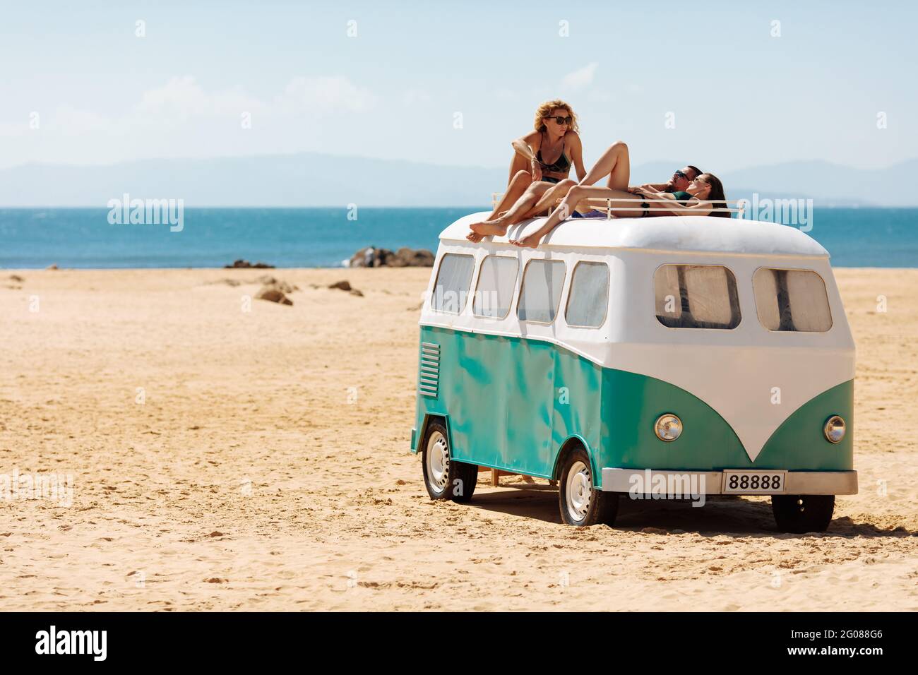 Gruppo di turisti che si rilassano in cima all'hippie bus sulla spiaggia Foto Stock