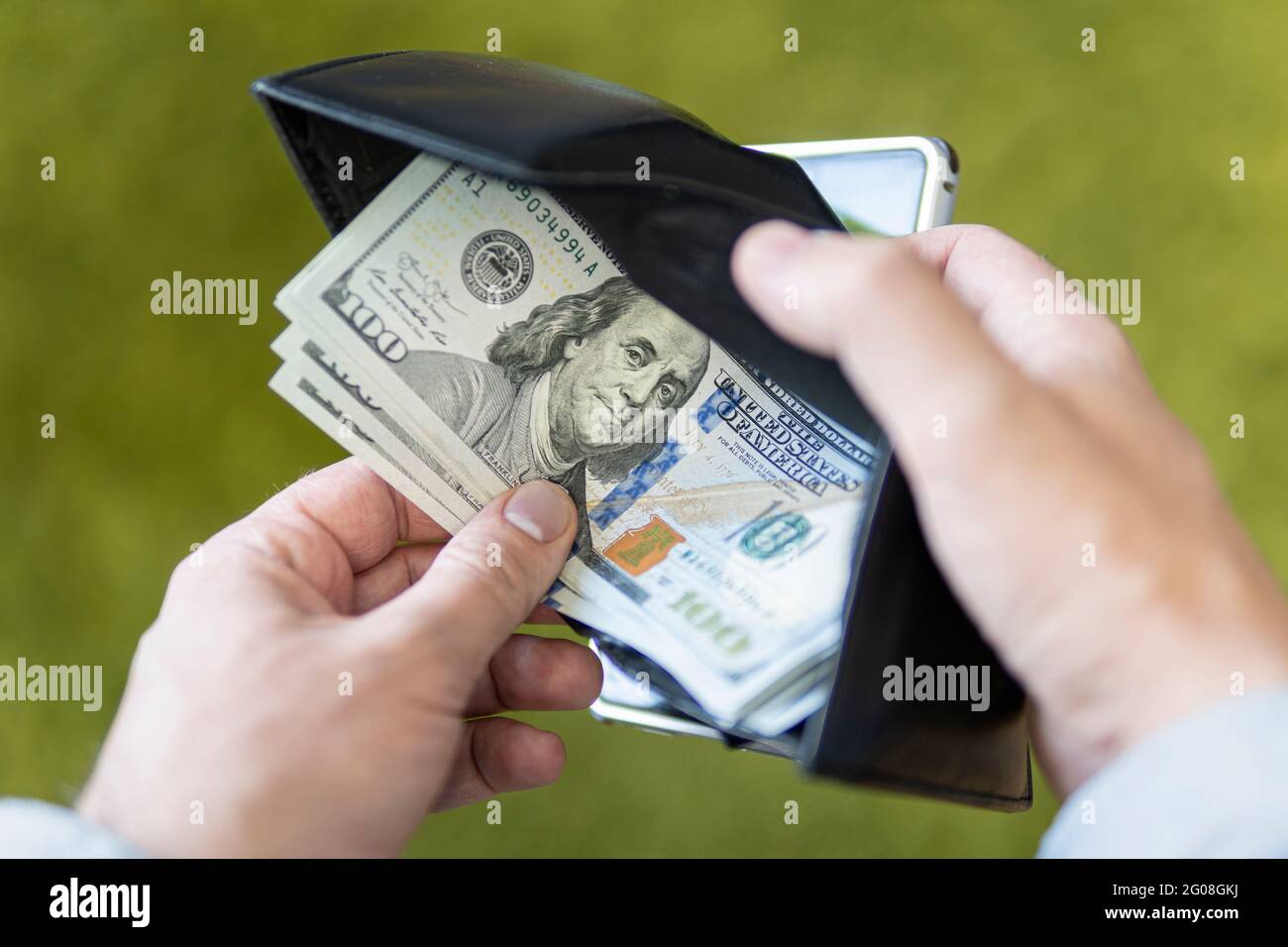 Borsetta con dollari nelle loro mani. Un uomo d'affari maschile apre un portafoglio nero e tira fuori un conto di cento dollari su uno sfondo verde. Stipendio del dipendente. Foto Stock