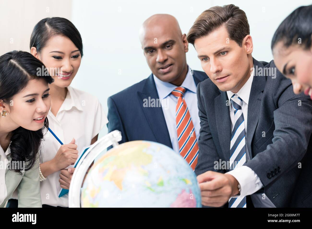 La gente di affari in riunione sulla strategia di discutere nuovi mercati guardando un mappamondo Foto Stock