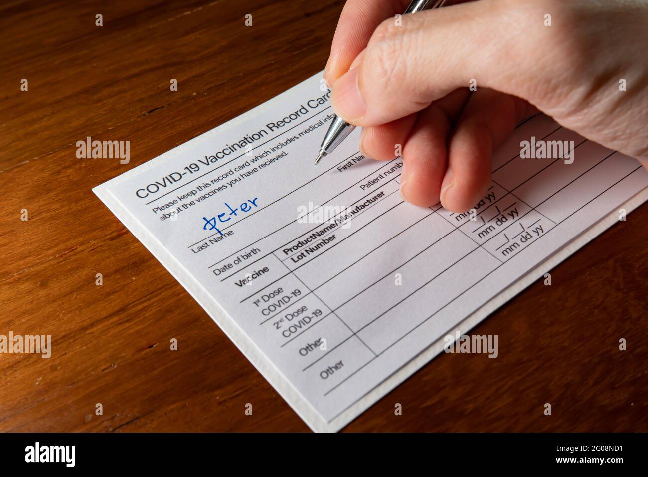 Scrittura di un nome su una scheda di registrazione della vaccinazione Covid-19 Foto Stock