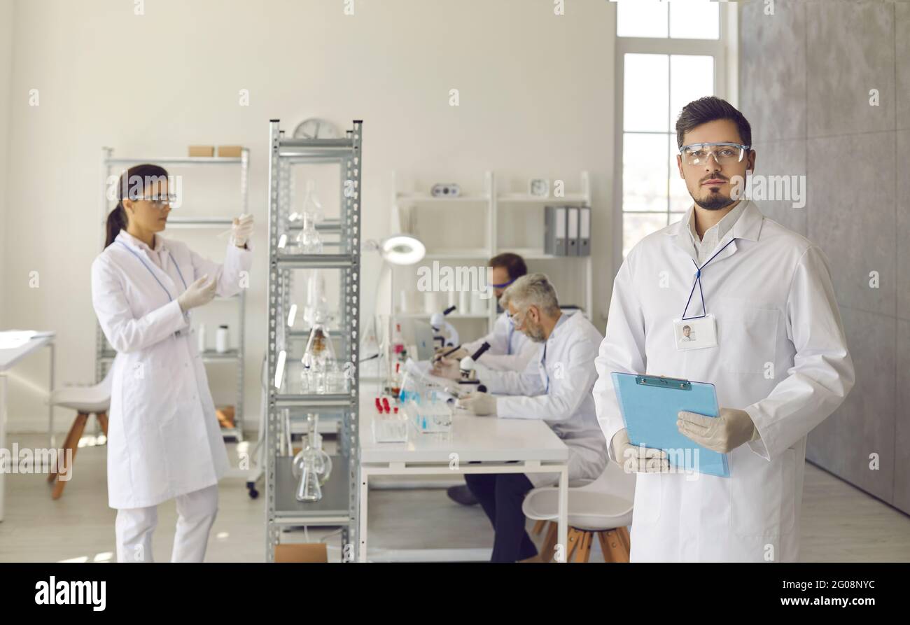 Ritratto di scienziato in laboratorio di scienze della vita con il team che lavora sullo sfondo Foto Stock