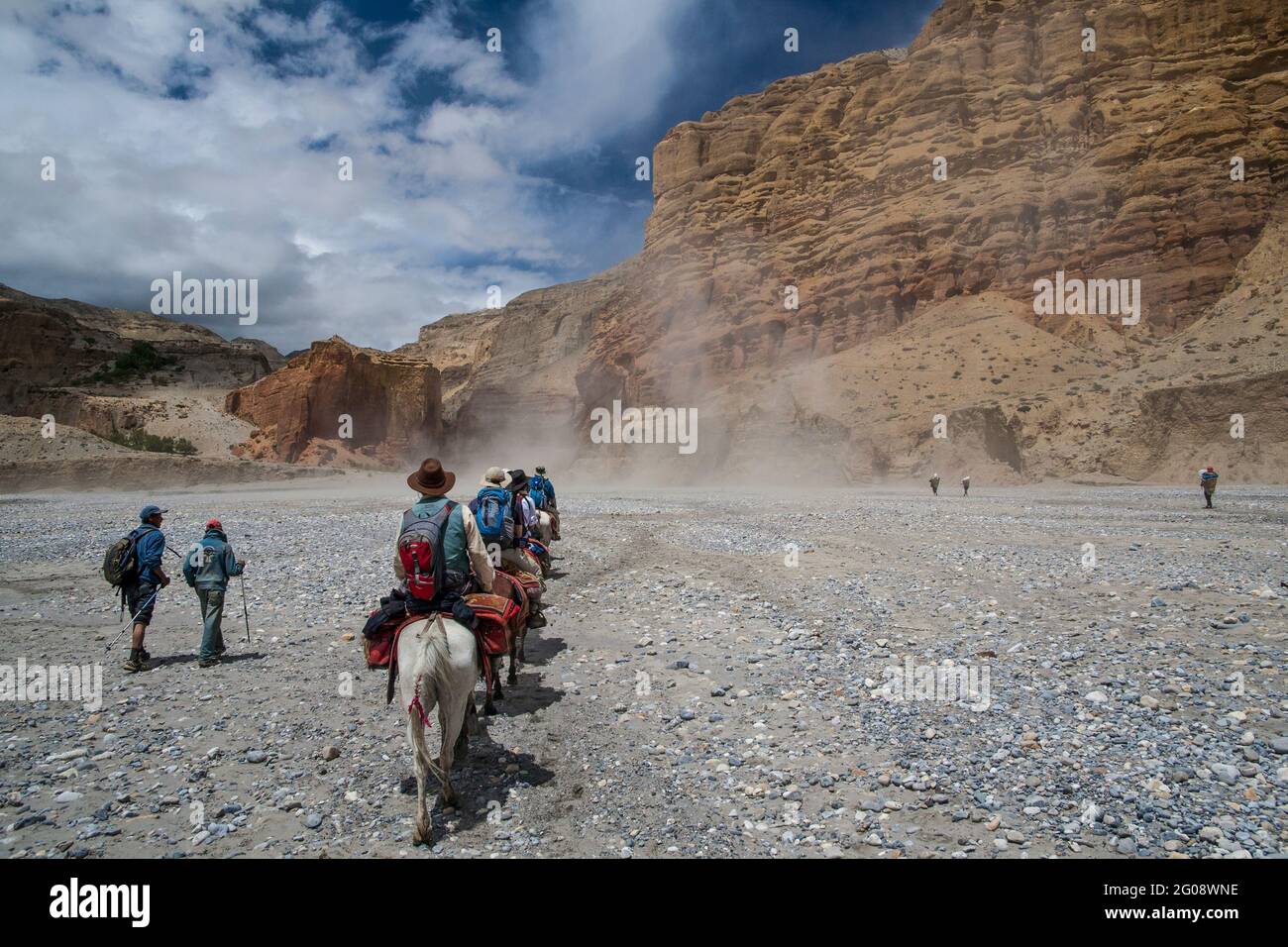 Una tempesta di polvere si snoda intorno ai pedoni che cavalcano i pony verso il villaggio di Chele lungo il letto del fiume Kali Gandaki. Foto Stock