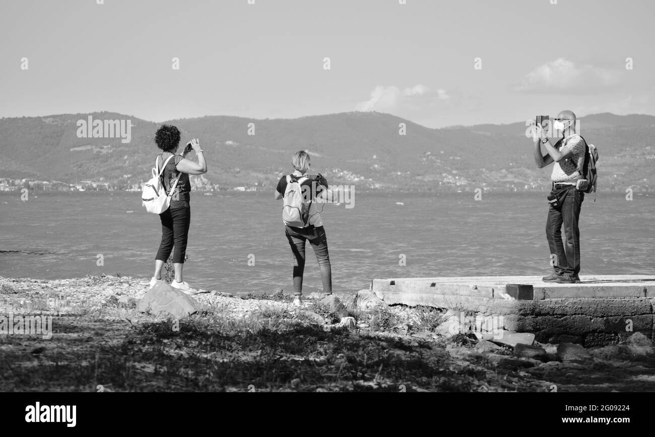 Maggio 2021, persone mature con maschera di salute fotografia con il loro smartphone panoramiche sulla riva del lago Trasimeno Foto Stock