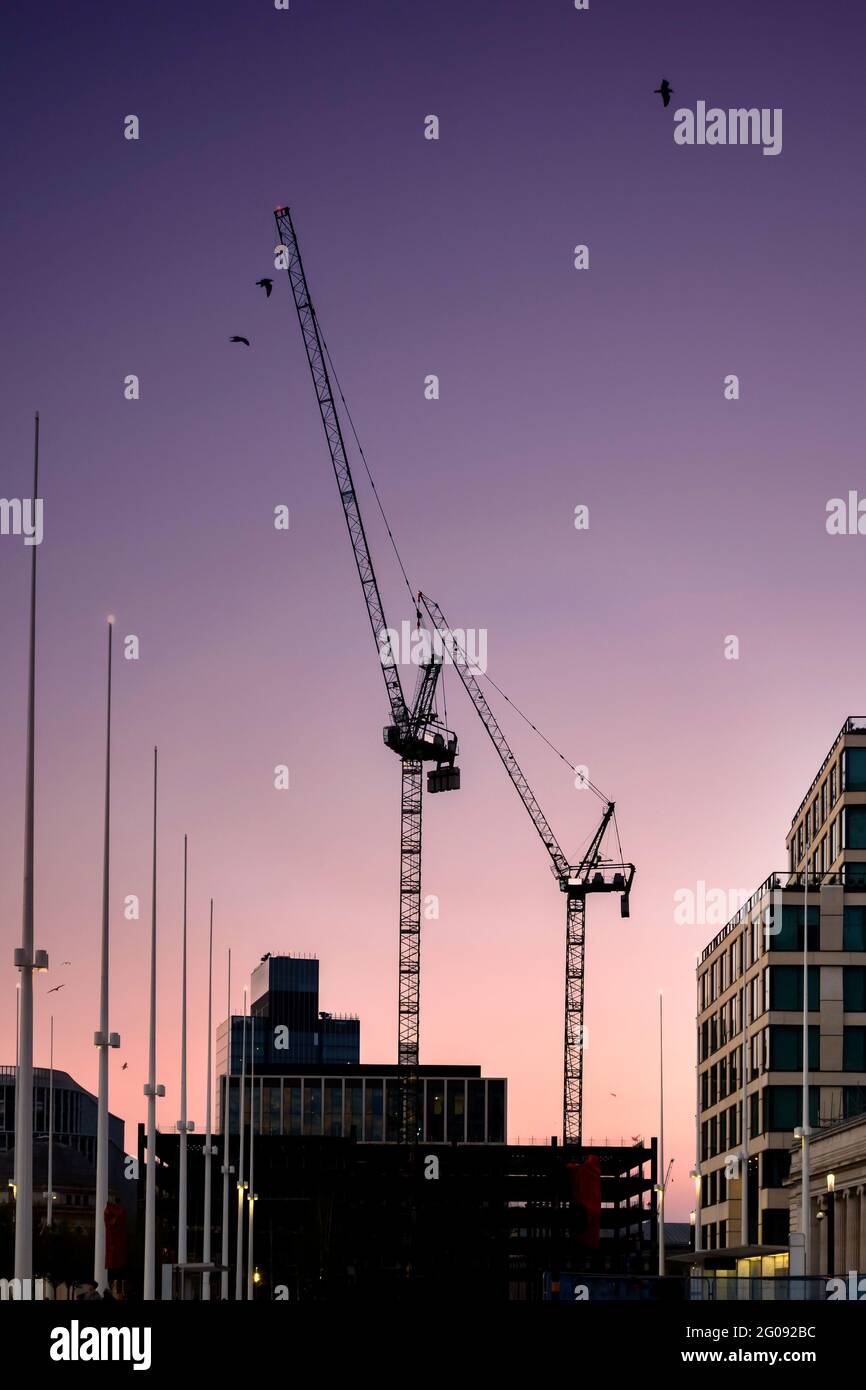 Moderne gru a torre che costruiscono nuovi edifici al tramonto nel sito di costruzione della città con il bel cielo arancione dell'alba. Sagoma della gru Foto Stock