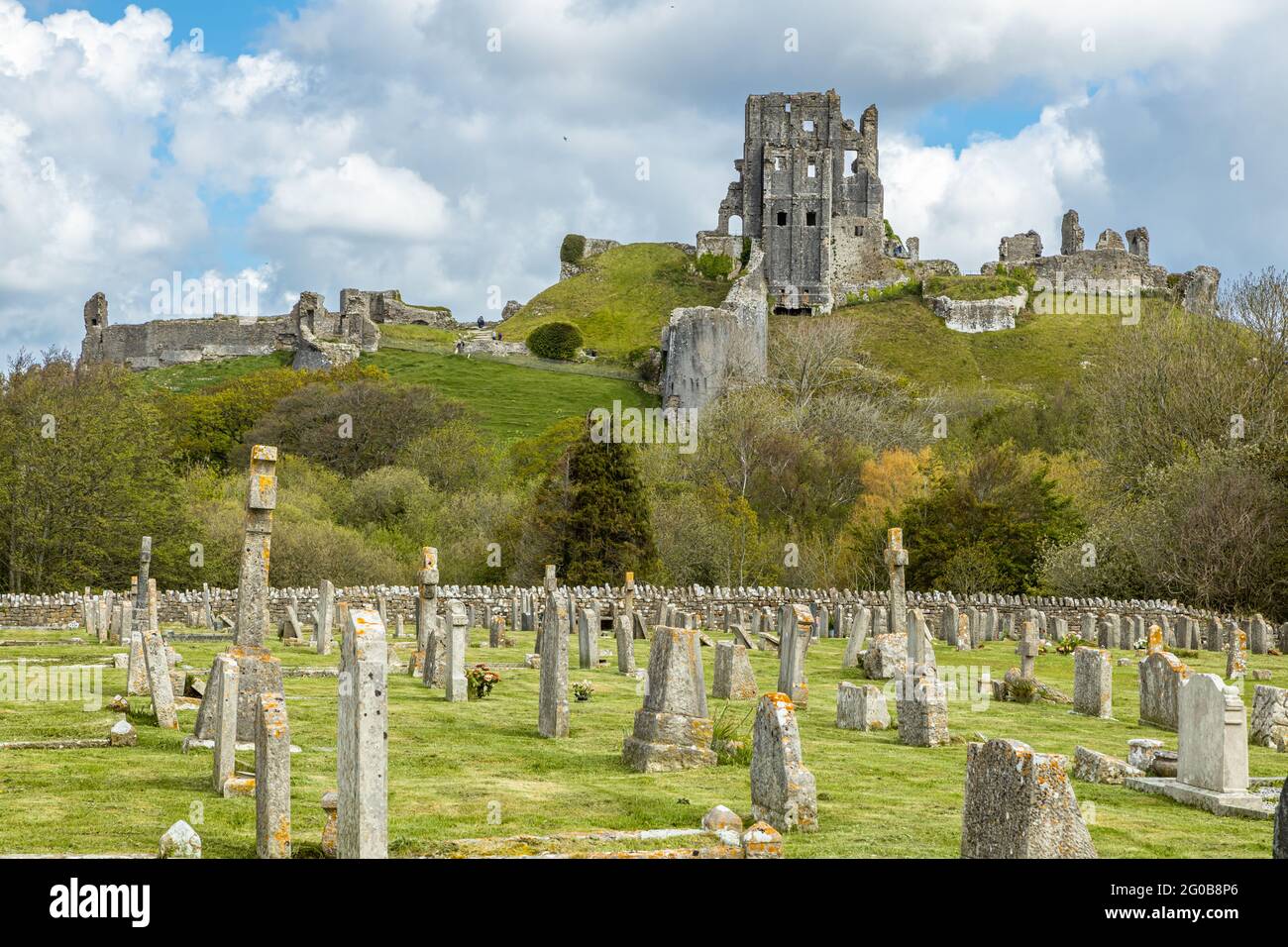 Lapidi nel cimitero del castello di Corfe con le rovine del castello di Corfe che si innalzano sopra le Purbeck Hills, Dorset, Inghilterra Foto Stock