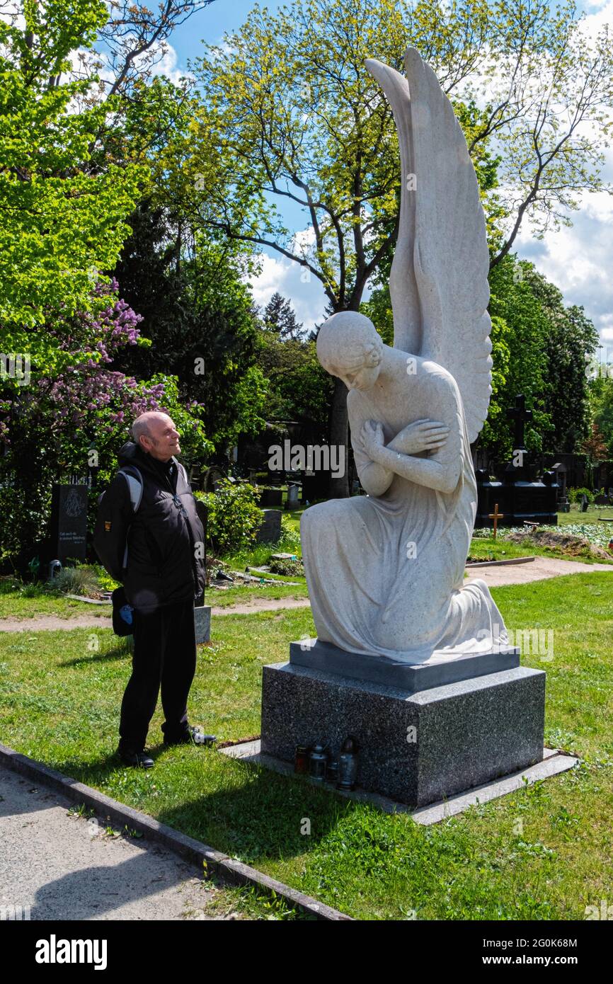 L'uomo anziano si trova accanto all'angelo di marmo all'ingresso del cimitero di St. Hedwig, Alter Domfriedhof St. Hedwig, Berlino. Foto Stock
