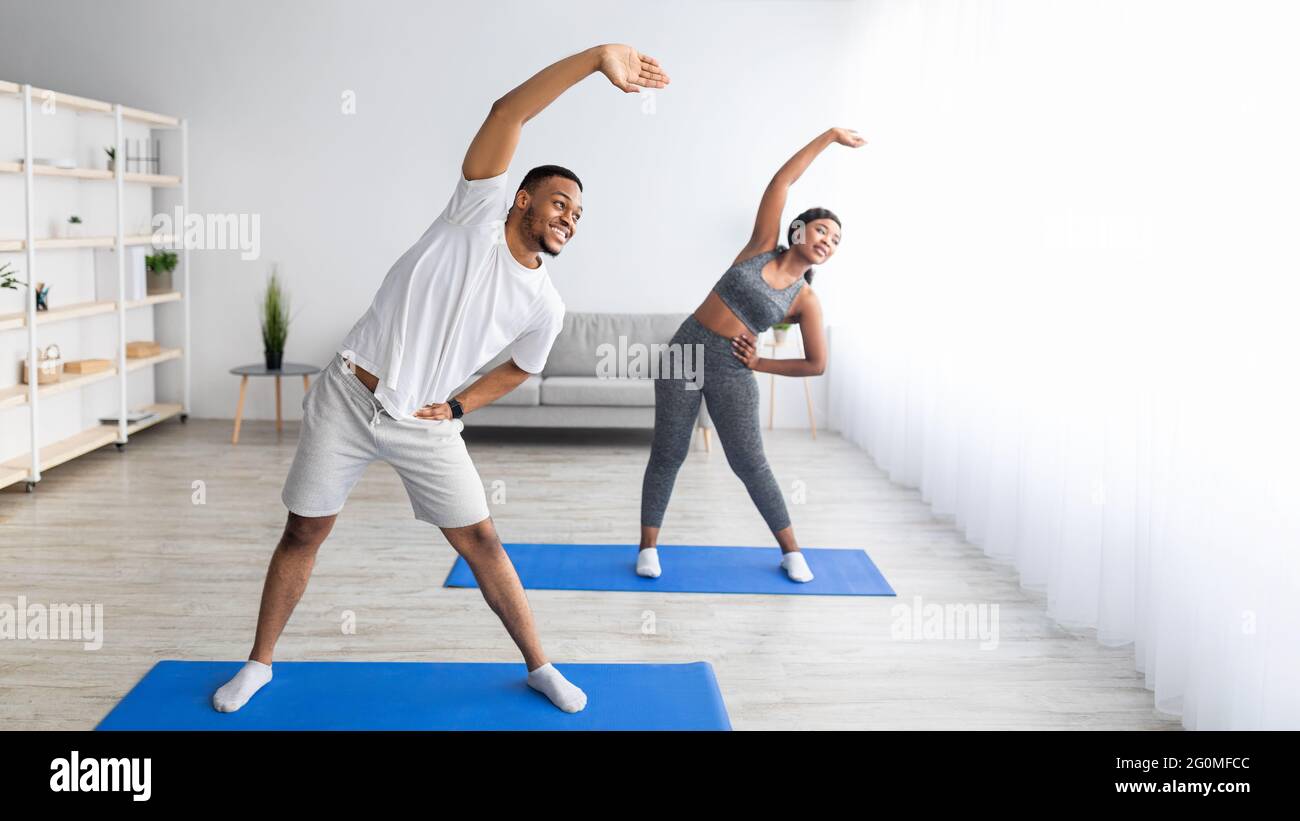 Coppia nera atletica che si piega da parte, facendo esercizi a casa, banner design con spazio libero Foto Stock