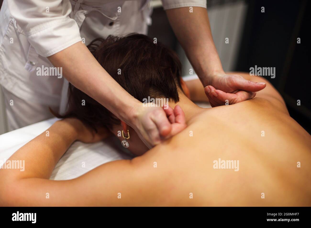 Master senza volto che dà massaggio di muscoli della schiena e delle spalle a. donna anonima sdraiata sul tavolo nel salone termale Foto Stock Master senza volto che dà massaggio di muscoli della schiena e delle spalle a. donna anonima sdraiata sul tavolo nel salone termale Foto Stock