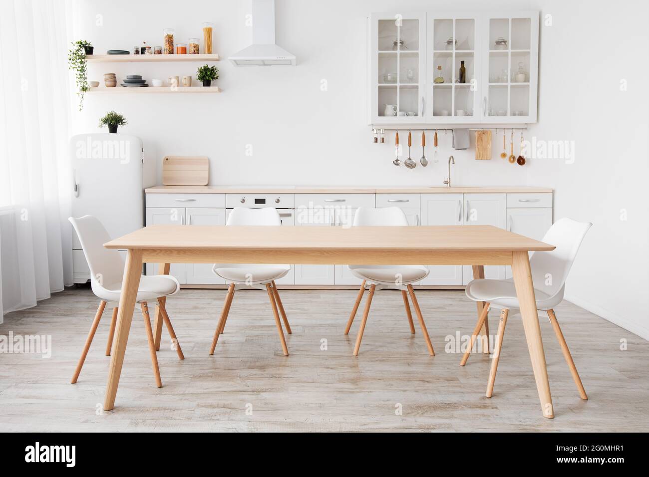 Luminosa cucina bianca con articoli per la casa. Interni moderni con cucina, tavolo e sedie in legno nella sala da pranzo Foto Stock