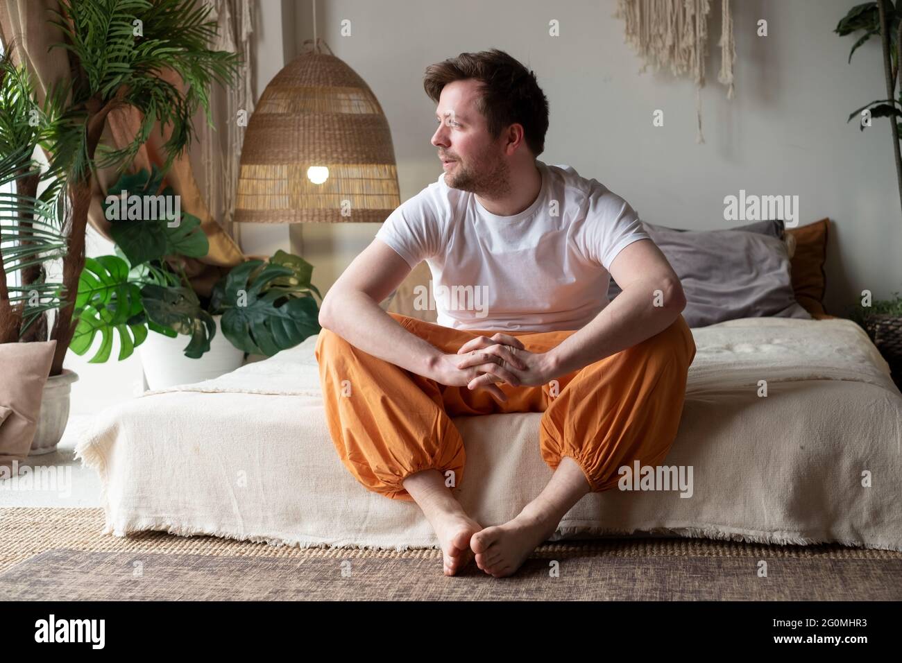 Sorridente giovane uomo seduto sul suo letto mentre guardando la telecamera Foto Stock
