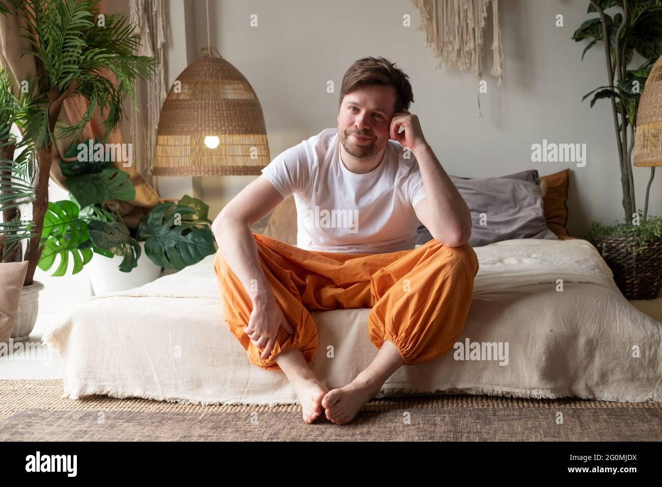 Sorridente giovane uomo seduto sul suo letto mentre guardando la telecamera Foto Stock