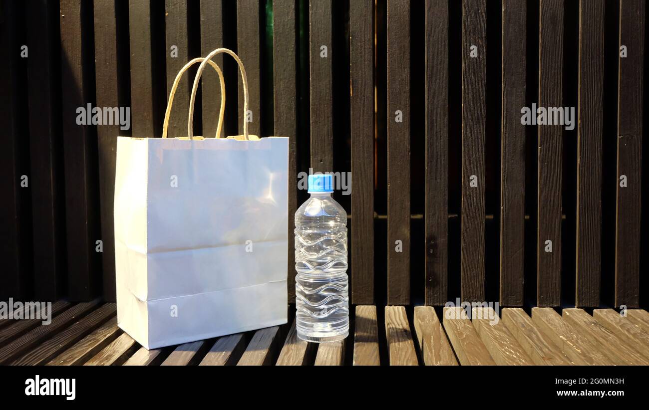 Una borsa per la spesa in carta bianca e una bottiglia d'acqua in plastica trasparente posta su un banco di legno, con fondo in legno. Con lo spazio per la copia sulla destra. Foto Stock