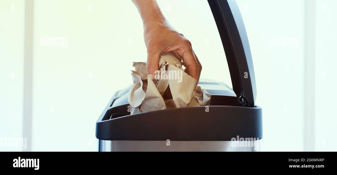 un giovane che lancia una palla di carta nel vano di carta e cartone di un cestino domestico di riciclaggio, in un formato panoramico da utilizzare come banner web o hea Foto Stock