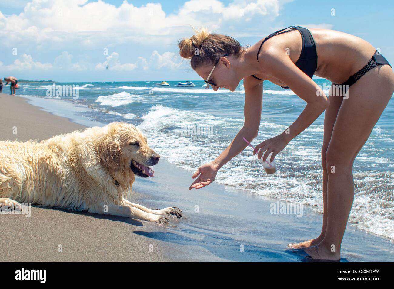 Giovane donna che sorride e gioca con il suo labrador sulla spiaggia di sabbia Foto Stock