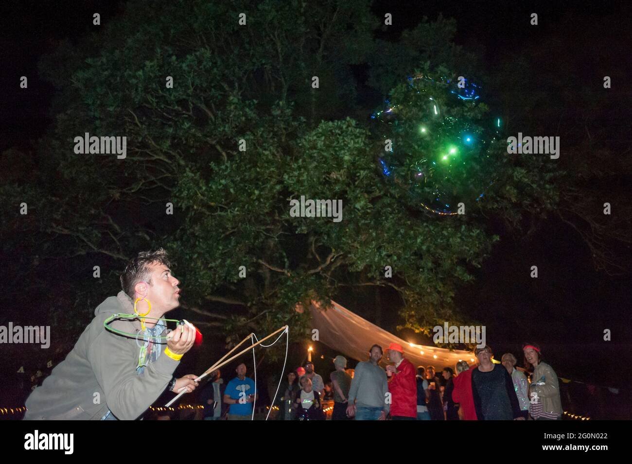 Un uomo soffia grandi bolle nel cielo di notte in un festival estivo Foto Stock