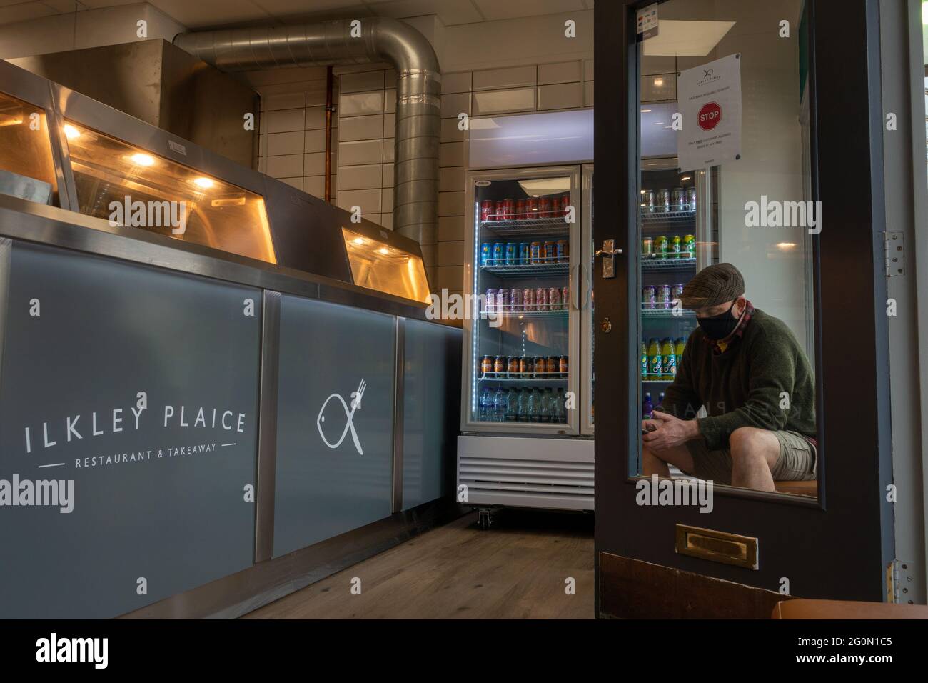 All'interno di un nuovo negozio di pesce e patatine (con una persona che indossa una maschera e cappellino piatto) a Ilkley che ha aperto durante la pandemia di Covid, Ilkley, West Yorkshire, U. Foto Stock