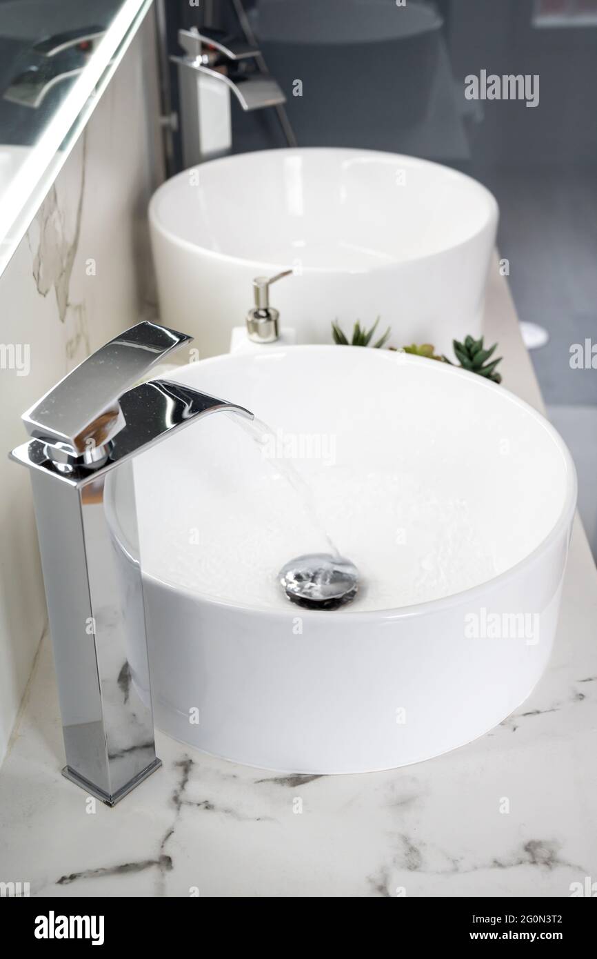 Due lavandini in ceramica all'interno di un bagno moderno e luminoso con specchio luminoso Foto Stock