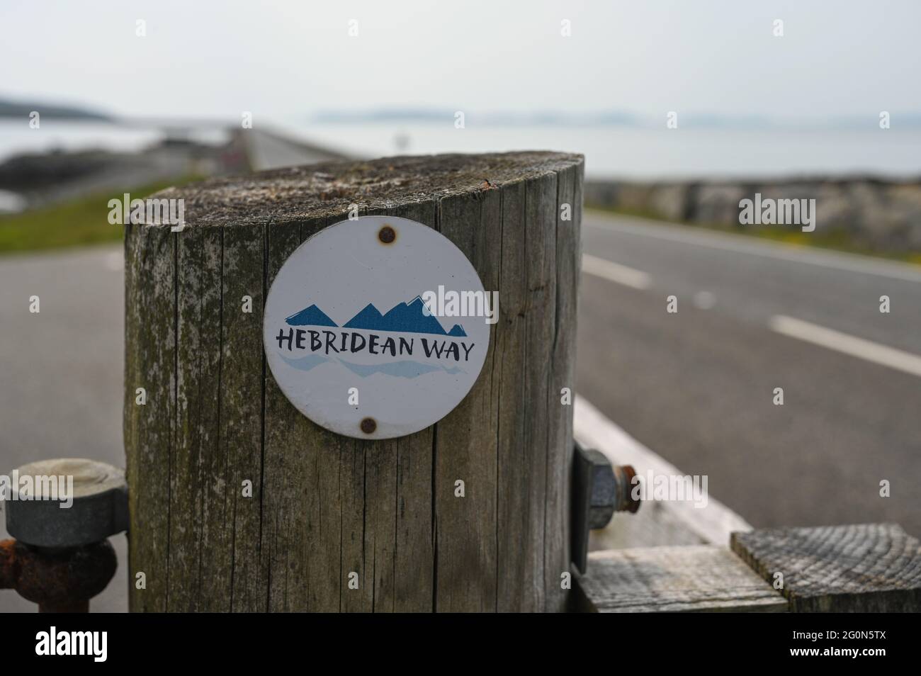 Via Ebridea segno su palo di legno. Sfondo molto offuscato della strada rialzata per Eriskay. Si tratta di un famoso percorso ciclistico e a piedi. Foto Stock
