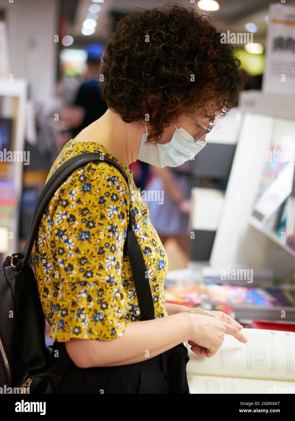 Una donna che guarda i libri in una libreria indossa una maschera facciale che la protegge dai virus Foto Stock