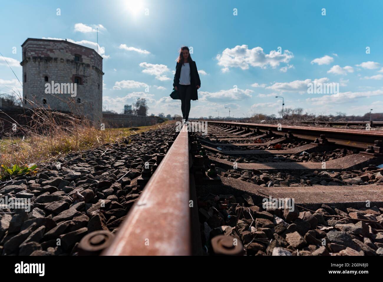 Giovane donna che cammina sulle piste ferroviarie con la torre Kula Nebojsa sullo sfondo Foto Stock