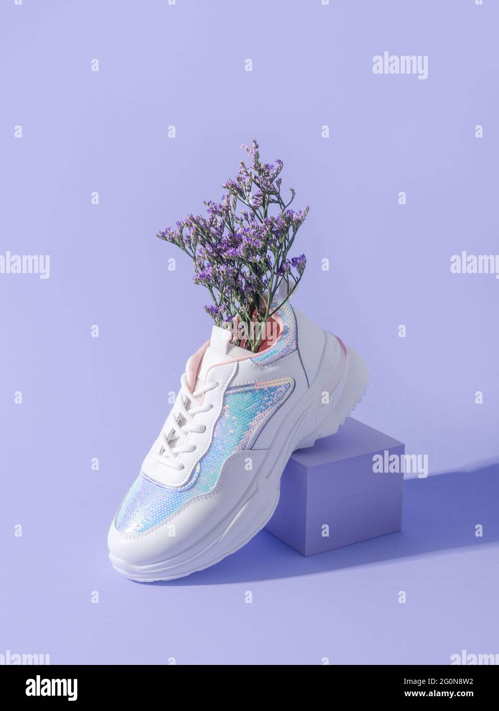 Sneakers femminili bianche con paillettes con fiori all'interno su sfondo  viola con podio a cubo geometrico Foto stock - Alamy