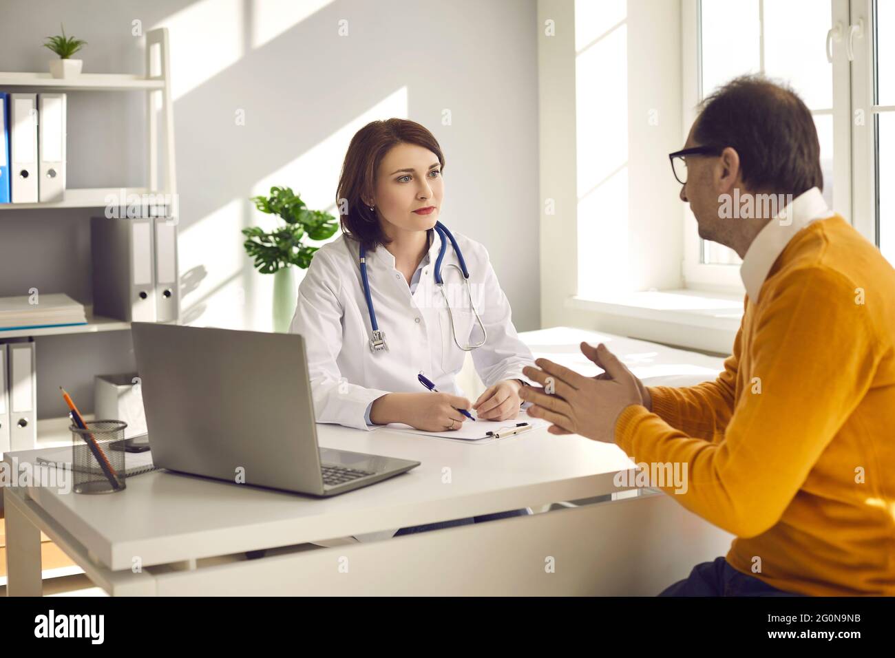 Paziente maschile di mezza età in un reparto ospedaliero consulta una dottoressa sulla sua salute. Foto Stock