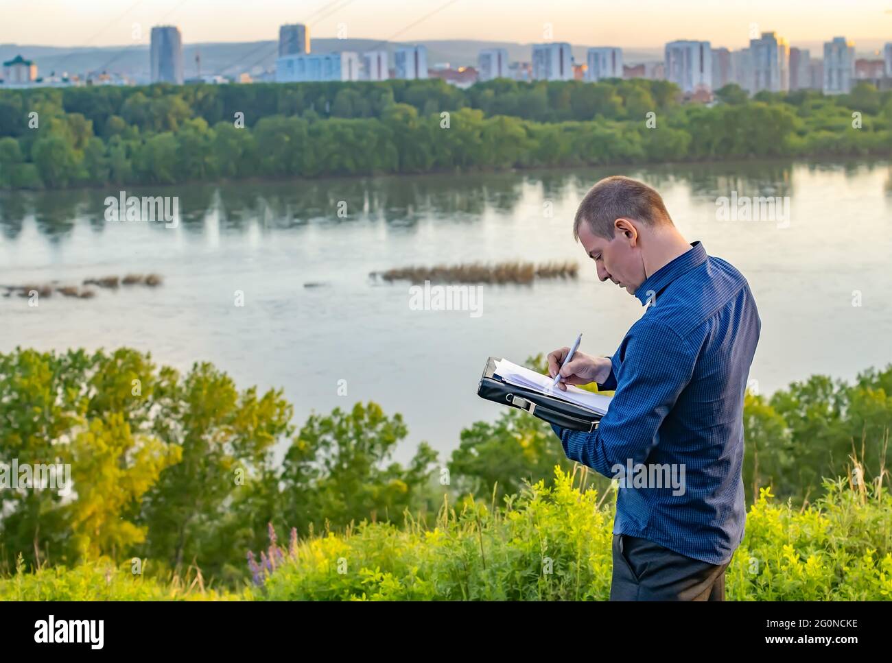 un uomo scrive su un pezzo di carta mentre si trova su una collina sulla riva Foto Stock