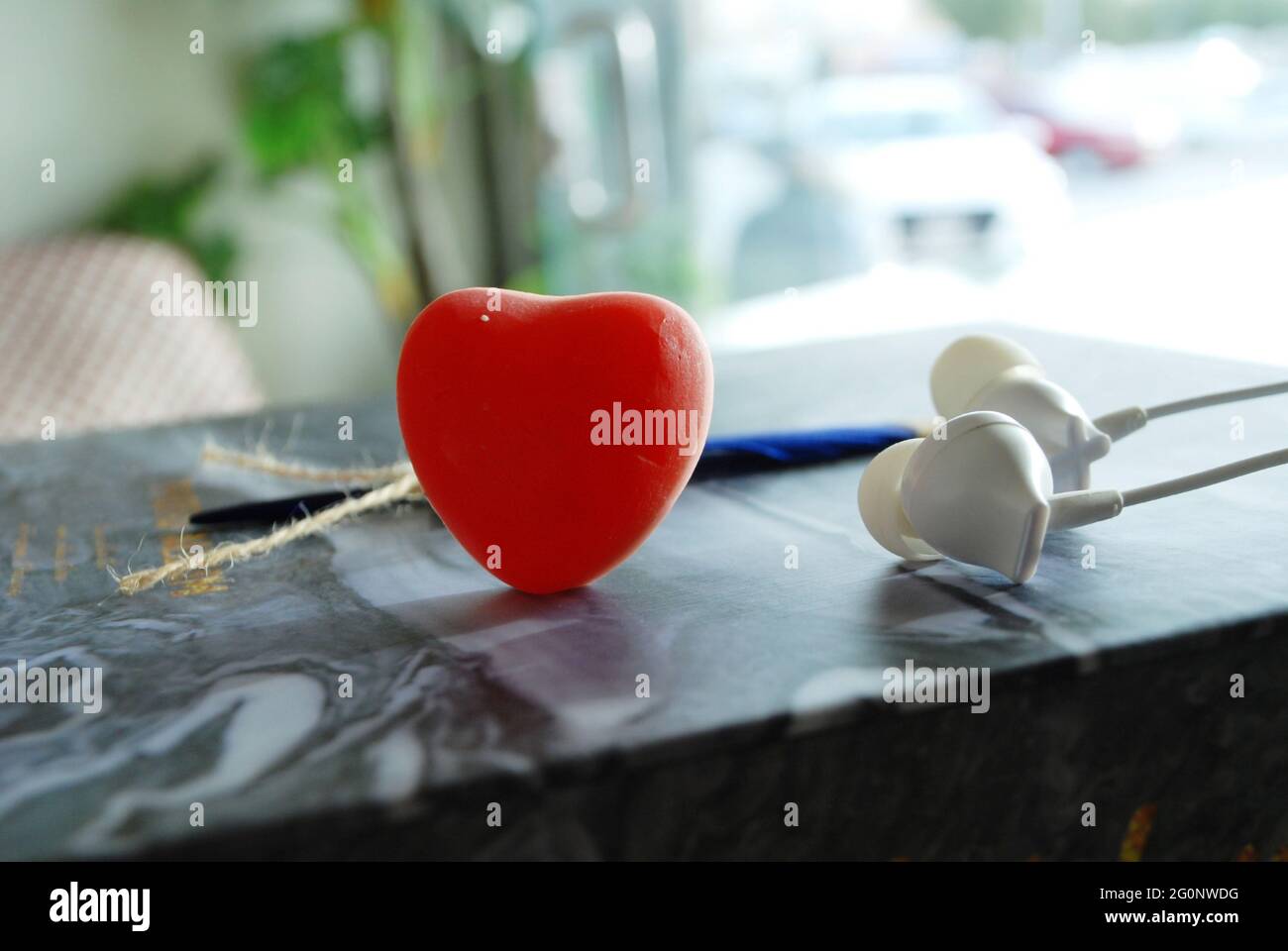 cuore di gelatina rossa con piuma blu e auricolari isolati carta ondulata in marmo, sfondo sfocato della luce del giorno, sfondo romantico, spazio per qoutes e testo Foto Stock